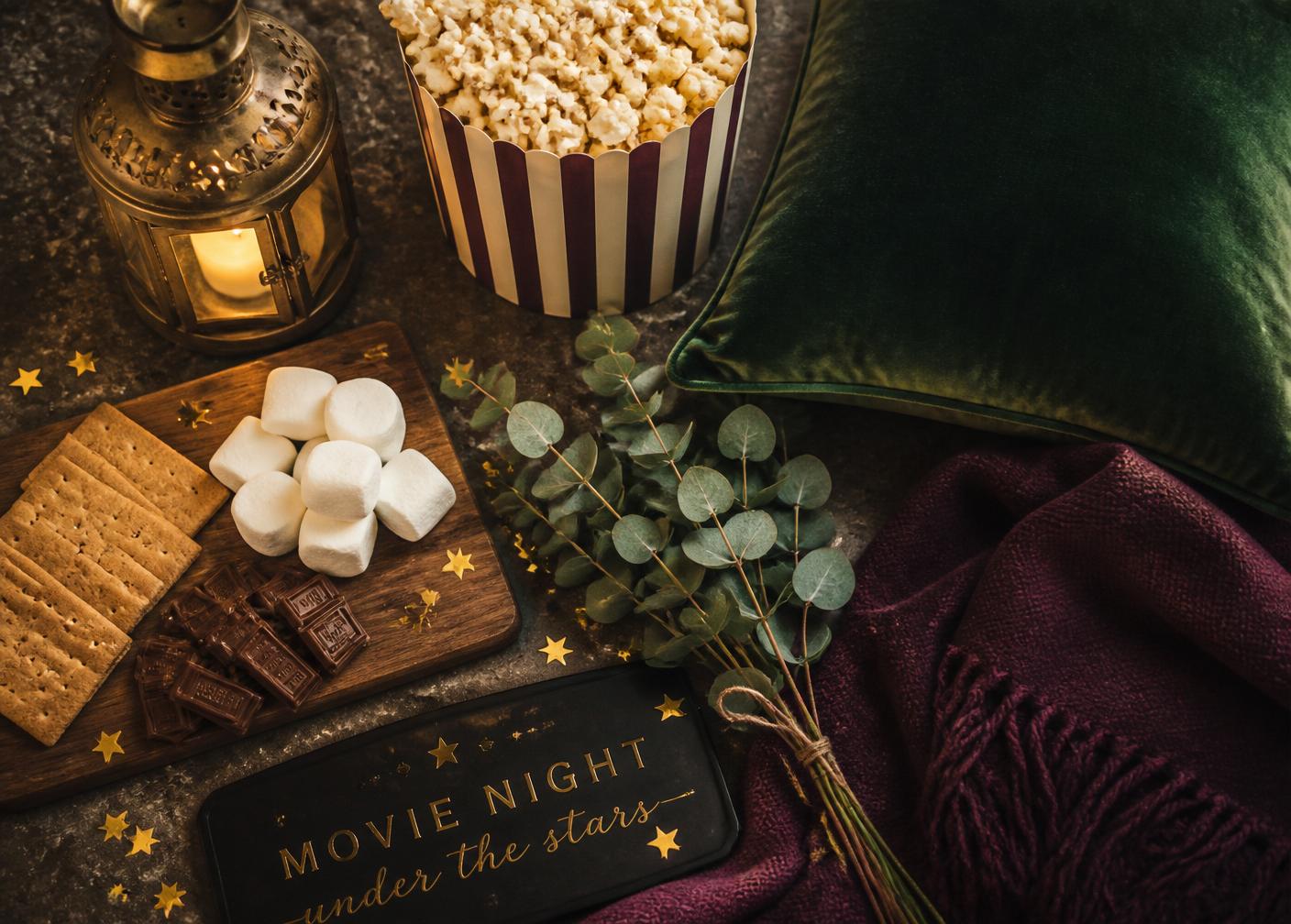 Flatlay of popcorn, velvet pillows, lantern, s'mores ingredients